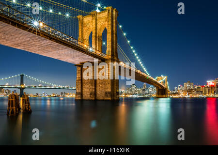 Illuminato il Ponte di Brooklyn da notte come visto dal lato di Manhattan - molto lunga esposizione per una superficie perfettamente liscia acqua Foto Stock