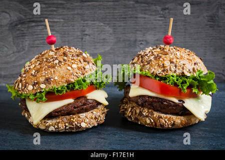 Due hamburger gourmet con il formaggio svizzero e verdure fresche sulle ciambelle multigrain su sfondo scuro Foto Stock