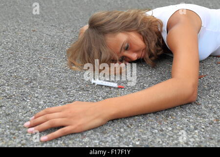 Un farmaco-addicted adolescente wirh siringa giacente su una strada Foto Stock