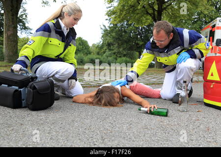 Un adolescente ubriaco sul pavimento con personale paramedico Foto Stock