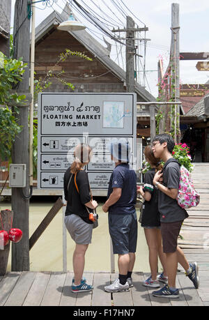 Turisti asiatici leggere un segno multilingue al mercato galleggiante, una attrazione turistica di Pattaya, Thailandia, Sud est asiatico Foto Stock