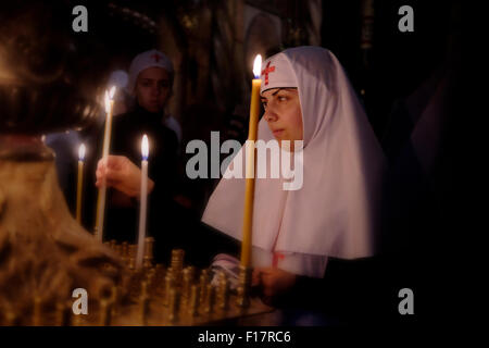 Una suora ortodossa cristiana illumina le candele mentre prega all'interno della Chiesa del Santo Sepolcro, nella città vecchia di Gerusalemme Israele Foto Stock