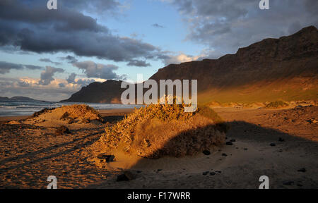 Spiaggia di Playa de Famara al tramonto con nuvole e catena montuosa Risco de Famara nell'estremo (Lanzarote, Isole Canarie, Spagna) Foto Stock