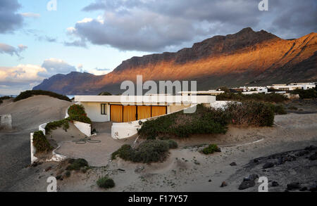 Bungalow a Playa de Famara dune al tramonto con la catena montuosa Risco de Famara sullo sfondo (Lanzarote, Isole Canarie, Spagna) Foto Stock