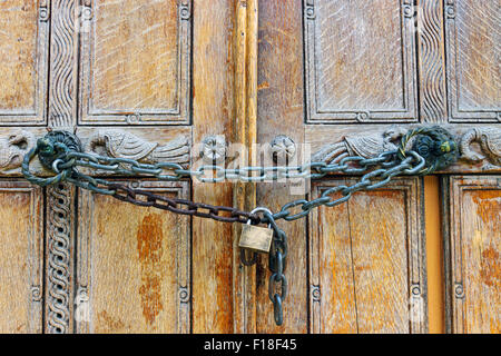 Una vecchia porta di legno bloccata da una catena con un lucchetto Foto Stock
