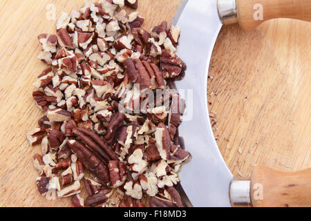 Close-up di noci pecan tostate e tritate su una tavola di legno con un coltello oscillante Foto Stock