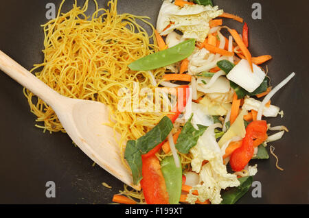 Primo piano di friggere ingredienti in un wok con un cucchiaio di legno Foto Stock