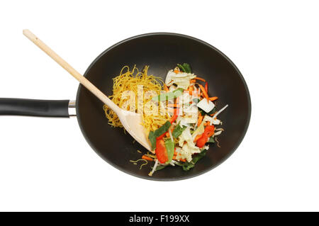 Friggere gli ingredienti con un cucchiaio di legno in un wok isolata contro bianco Foto Stock