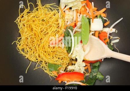 Primo piano di friggere ortaggi e Singapore tagliatelle con un cucchiaio di legno in un wok Foto Stock