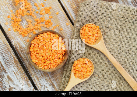 Non cotti di lenticchie rosse nella ciotola e su cucchiai di legno Foto Stock