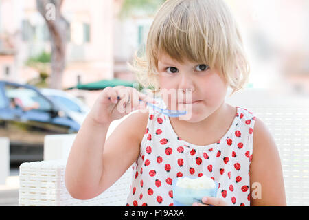 Caucasian Baby girl mangia yogurt congelato, closeup ritratto all'aperto con luce naturale Foto Stock