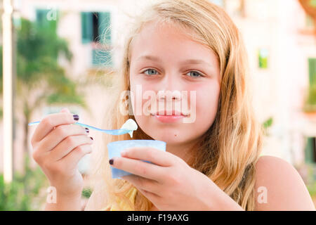 Bionda caucasica ragazza adolescente mangia yogurt congelato, chiudere fino all'aperto verticale con luce naturale Foto Stock