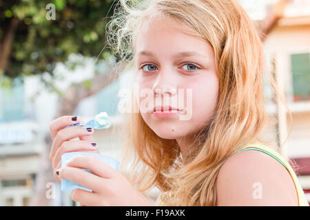 Bionda caucasica ragazza adolescente con yogurt congelato, closeup ritratto all'aperto con luce naturale Foto Stock