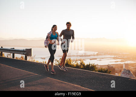 Coppia giovane jogging la mattina presto. Giovane uomo e donna in corsa all'aperto sul lato di una collina strada. Foto Stock