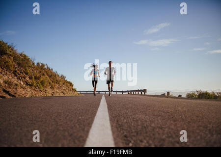 Basso angolo vista di due giovani in esecuzione su strada. Coppia giovane jogging insieme sulla strada di campagna sulla giornata estiva con un sacco di cop Foto Stock