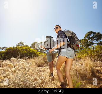 I giovani facendo un dislivello in salita durante le escursioni in campagna. Donna con mappa guardando indietro sopra la sua spalla sorridendo con uomo wa Foto Stock
