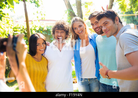 Mani femminili tenendo la fotocamera digitale e rendendo la foto di un gruppo di amici Foto Stock