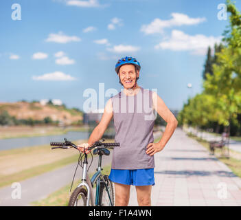 Attivo uomo senior in posa con la sua bicicletta e in piedi su un marciapiede esterno shot con inclinazione e spostamento lente Foto Stock