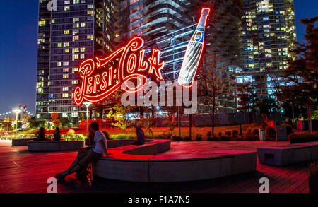 Giovane seduto inondate di luce rossa dal gigante neon di Pepsi Cola segno ,Gantry Plaza del Parco Statale di Long Island City NY Foto Stock