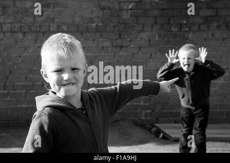 Bambini litigare e eccitante tra due ragazzi (fratelli, amici) all'aperto vicino red muro di mattoni Foto Stock