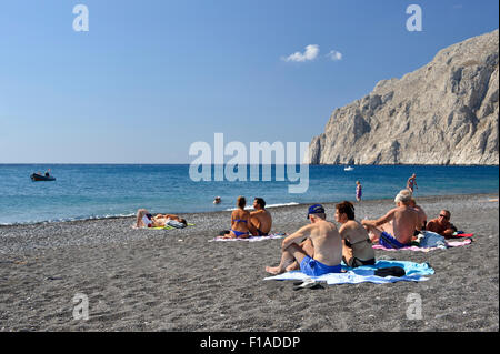 I turisti a prendere il sole su Kamari spiaggia di sabbia nera, Santorini, Grecia. Foto Stock