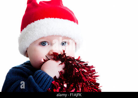 Un studio shot del bambino contro uno sfondo bianco che indossa un cappello di Natale e azienda tinsel Foto Stock