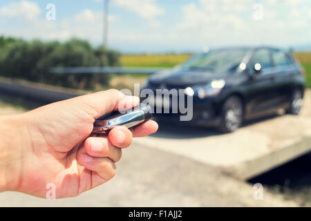 Primo piano di un giovane uomo lo sbloccaggio delle porte della sua vettura con il comando a distanza di chiave, all'aperto, con un effetto di filtro Foto Stock