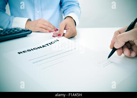 Primo piano della mano di un uomo che è la firma di un documento di dimissioni su una scrivania di fronte a una giovane donna Foto Stock