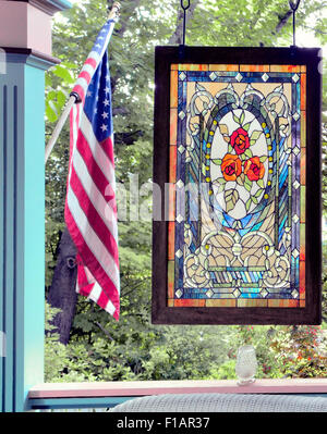 Una vetrata decorativa in stile Art Nouveau presenta un medaglione ovale centrale con tre rose rosse e arancioni, incorniciate da scrolli ornati Foto Stock