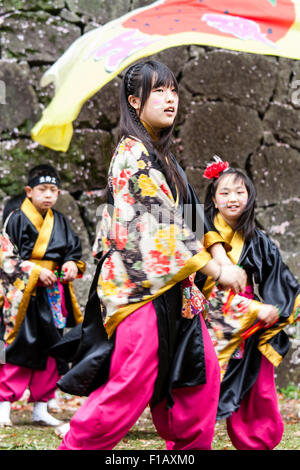 Kumamoto, Giappone, Yosakoi Festival. Corpo di ballo di bambini, 10-16 anni, tenendo naruko e in nero happi coats, ballare nella parte anteriore del muro di castello Foto Stock