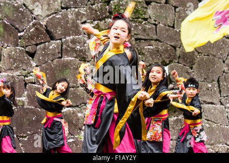 Kumamoto, Giappone, Yosakoi Festival. Corpo di ballo di bambini, 10-16 anni, tenendo naruko e in nero happi coats, ballare nella parte anteriore del muro di castello Foto Stock