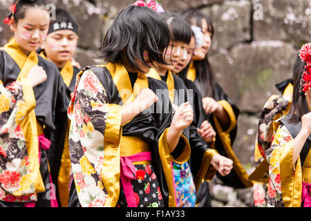 Kumamoto, Giappone, Yosakoi Festival. Corpo di ballo di bambini, 10-16 anni, tenendo naruko e in nero happi coats, ballare nella parte anteriore del muro di castello Foto Stock