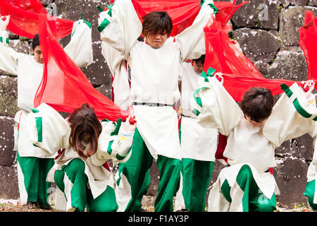 Giapponese Yosakoi dance team. Ballerini indossano il bianco e il verde costumi dancing mentre vorticoso panni rosso. Castello di parete in pietra dello sfondo. Foto Stock