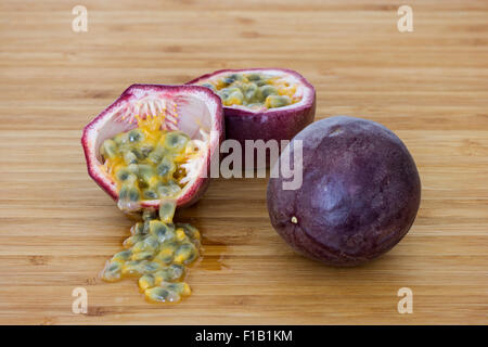 Close-up di un insieme e dividere i frutti della passione (granadiglie, viola granadilla (Passiflora edulis)), semi su un tavolo di legno. Foto Stock