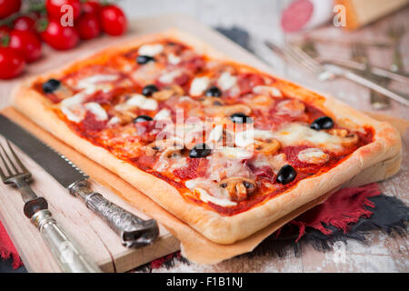 In casa rettangolare di salsiccia per pizza pizza su un tavolo rustico con ingredienti. Foto Stock