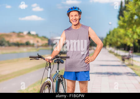 Attivo uomo senior in posa con la sua bicicletta e in piedi su un marciapiede esterno Foto Stock