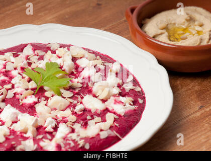 Purea di barbabietole con za atar spezie, yogurt e aglio guarnita con formaggio di capra e mandorle su una piastra di crema. Ciotola di hummu Foto Stock