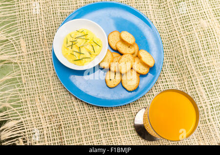 Piastra di colore blu con piccole fette di pane e burro rosmarino accanto al succo di arancia Foto Stock