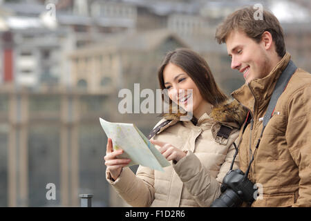 Coppia di turisti la consultazione di una guida in inverno con un background urbano Foto Stock