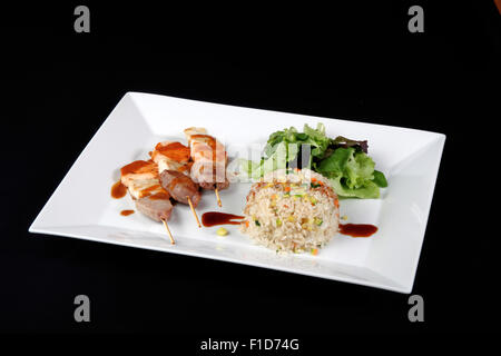 Menu di kebab con riso e verdure in piatto bianco su sfondo nero Foto Stock