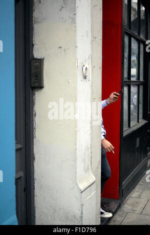 L'uomo texting sul suo telefono mobile e avente una sigaretta a Hoxton, East London Foto Stock