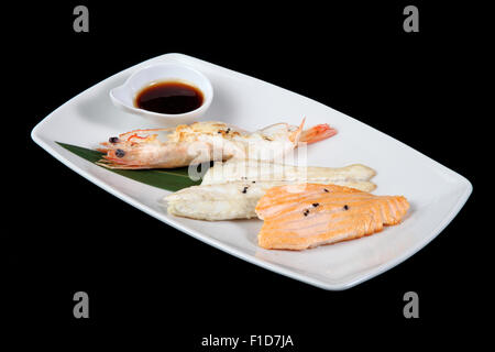 Misto di pesce alla griglia con salsa in piastra bianca su sfondo nero Foto Stock