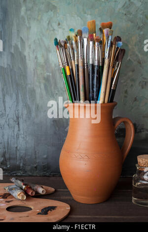 Pennelli in una brocca da potters argilla, palette, tubi di vernice e una bottiglia di olio in studio dell'artista. Foto Stock