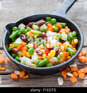 Verdure miste pasto nella vecchia padella closeup e gli ingredienti sul tavolo di legno. Foto Stock