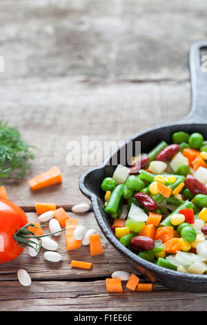 Verdure miste pasto in ferro vecchio padella closeup e ingredienti su legno tavolo rustico. Foto Stock