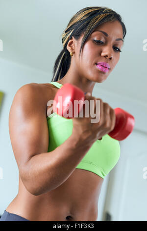 Giovane adulto americano africano donna in abbigliamento sportivo a casa, facendo fitness domestico e la formazione bicipite con il peso. Focus su Foto Stock