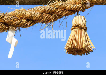 Il Giappone. Un Shide, bullone di illuminazione realizzato in carta appeso Shimenawa, un sacro dello Shintoismo paglia corda con uno sfondo di cielo blu. Foto Stock