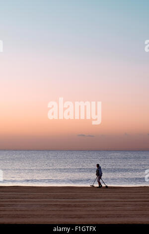 Uomo solitario con un rivelatore di metalli sulla St Aygulf beach (Francia) a sunrise. Foto Stock