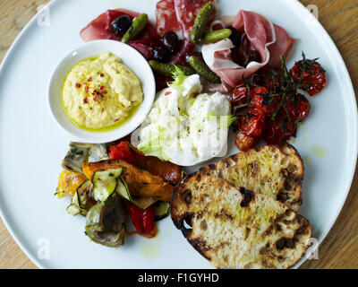 Un assortimento di prosciutti e verdure, serviti con salsa di pomodoro e il pane su una piastra bianca. Foto Stock