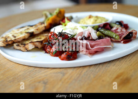 Un assortimento di prosciutti e verdure, serviti con salsa di pomodoro e il pane su una piastra bianca. Foto Stock